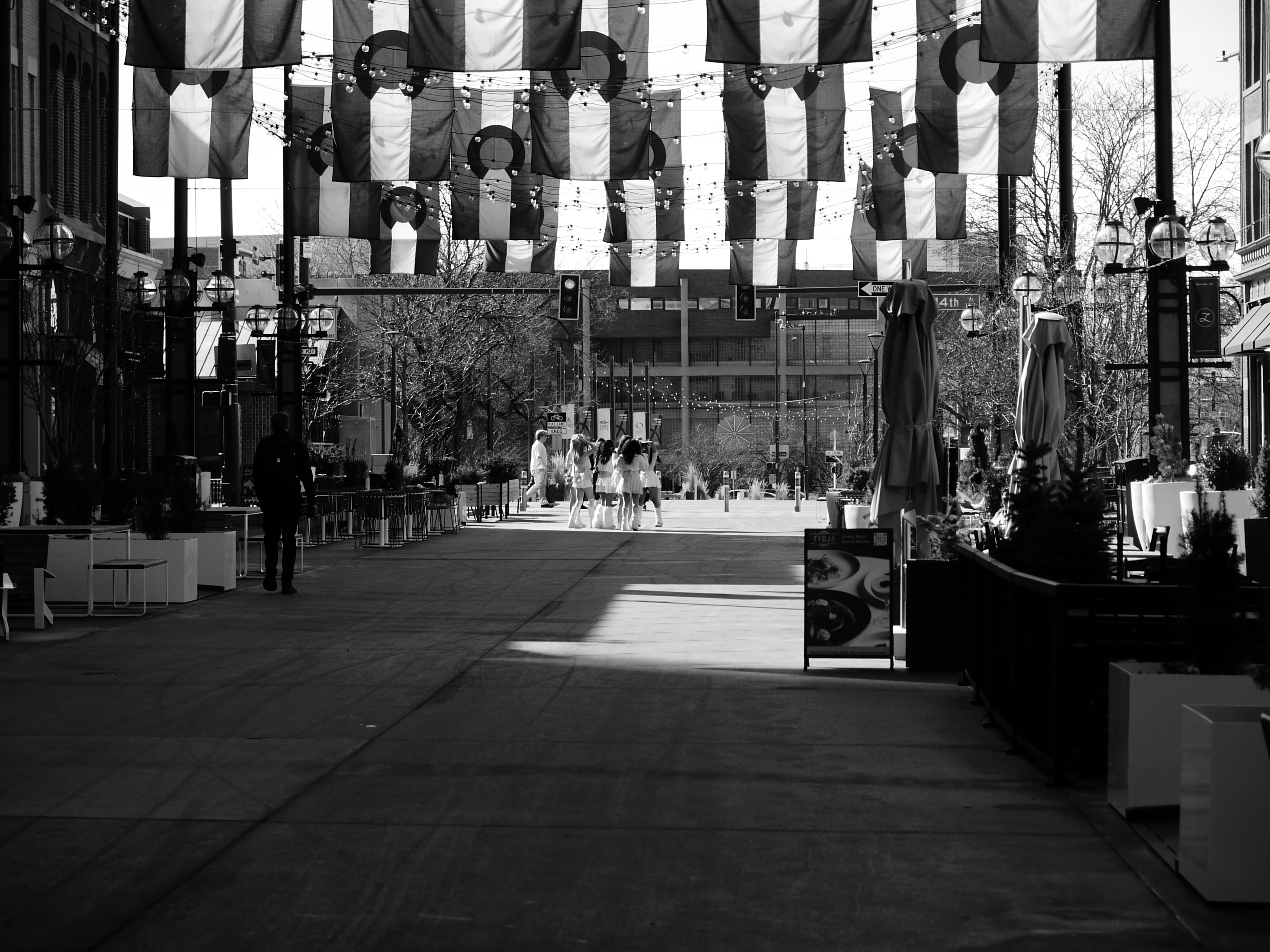 A street photo of a quiet commercial street with a group of people standing in the distance, shot on the Lumix L1