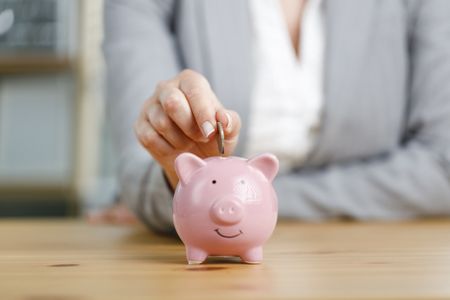 Businesswoman putting money into piggy bank. Concept of money saving and budgeting