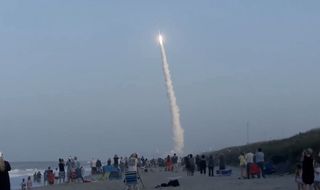 Beach-goers watch a United Launch Alliance Atlas V rocket launch into space carrying two military satellites on the AFSPC-11 mission. Liftoff occurred at 7:13 p.m. EDT on April 14, 2018.