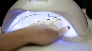 A woman with painted nails puts her hands under a UV lamp