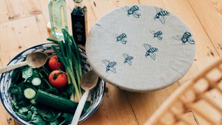 Bee printed linen food cover over bowl to show how to keep wasps away from food during summer dining