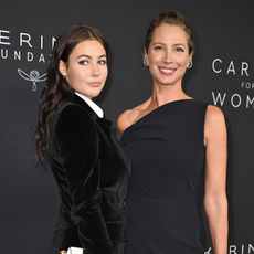 mother and daughter Christy Turlington and Grace Burns pose on the red carpet wearing a navy dress and velvet suit