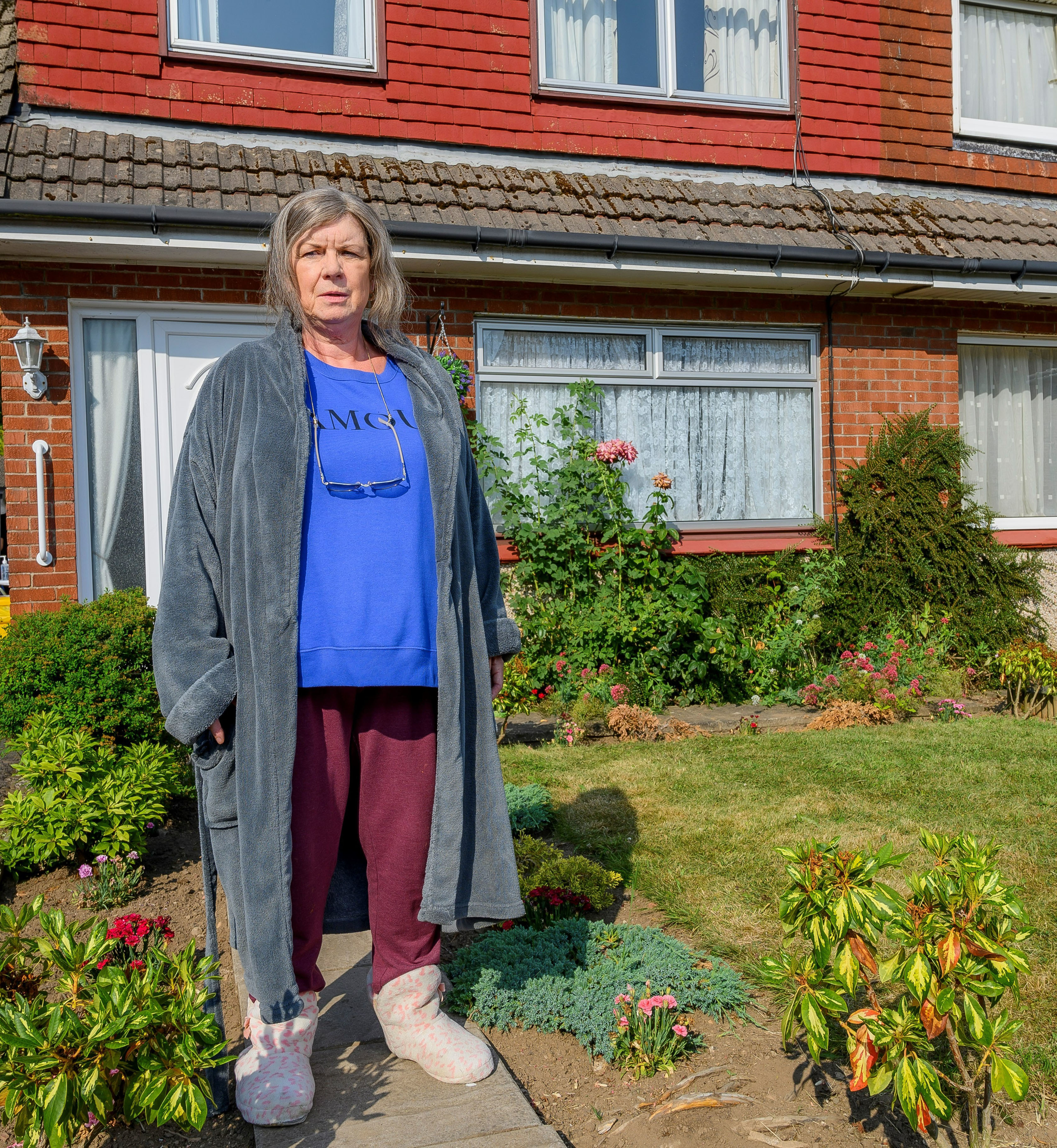 Christine in her garden wearing PJs, dressing gown and slippers.