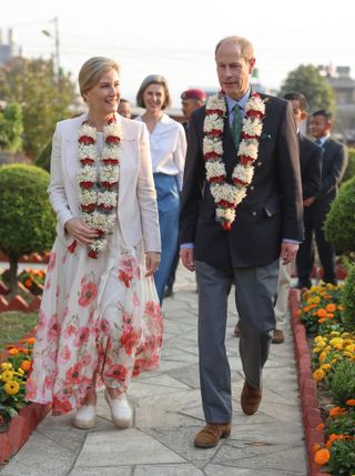 Duchess Sophie and Prince Edward wearing leis during a 2025 Nepal tour walking along a flower-lined path