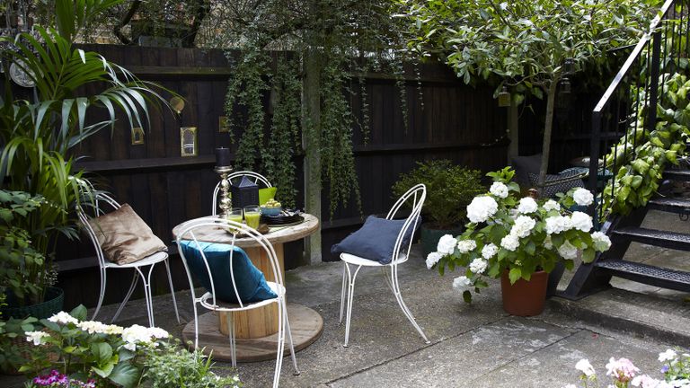 A concrete courtyard with round dining table and black fence and hydrangeas growing in pots