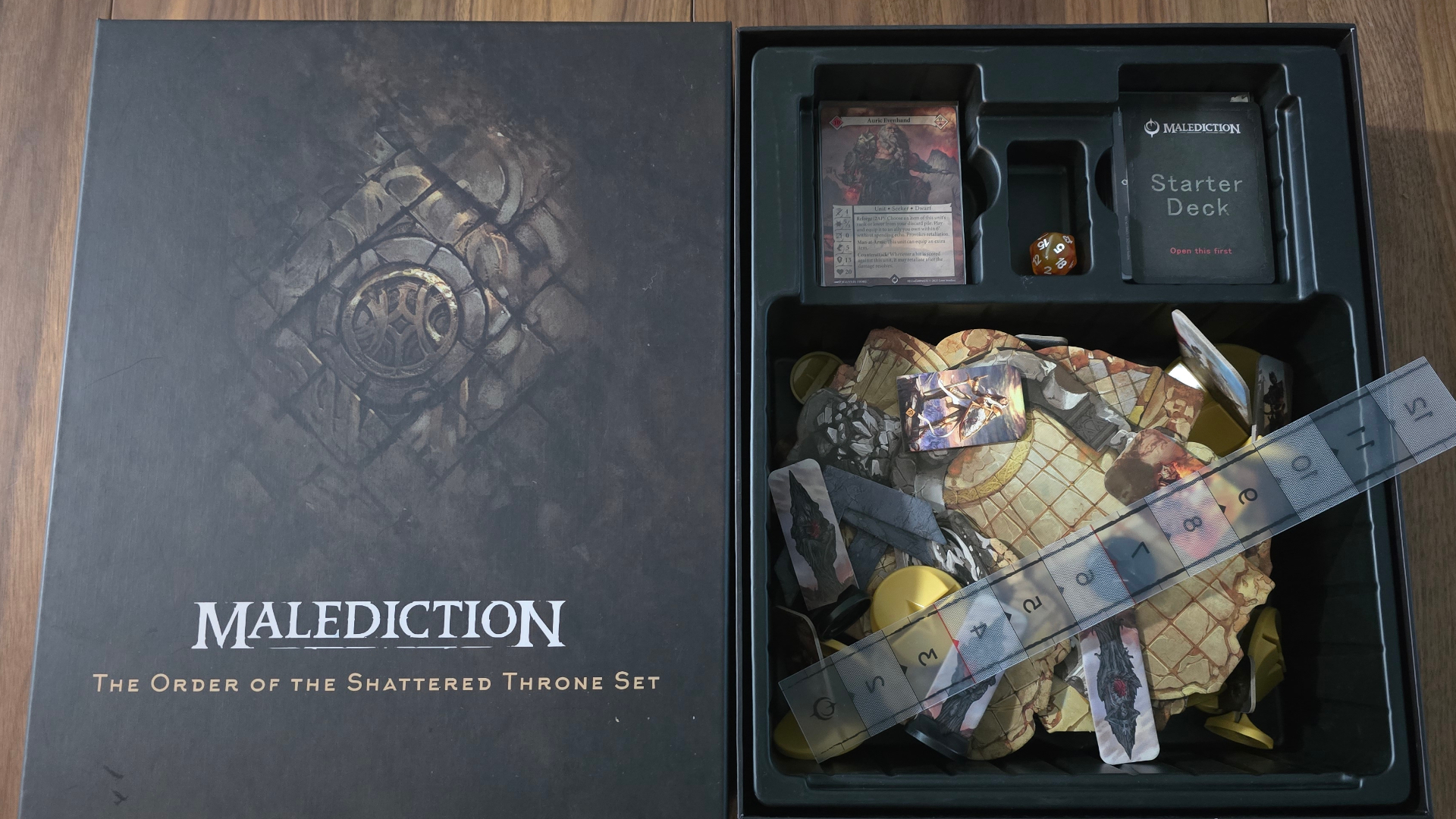 An open box for Malediction&#039;s The Order of the Shattered Throne, laid out on a wooden surface