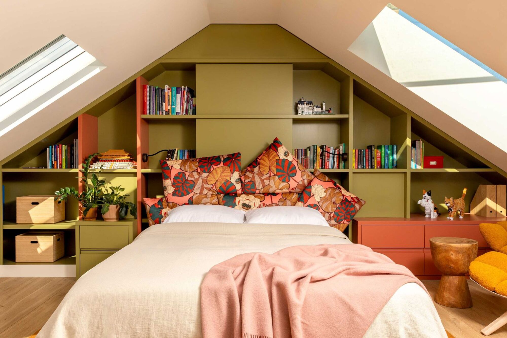colorful attic bedroom with green built-in cabinetry behind bed with colorful cushion headboard, white pillows, beige sheets, pink throw over the end of the bed, and skylights on the ceiling