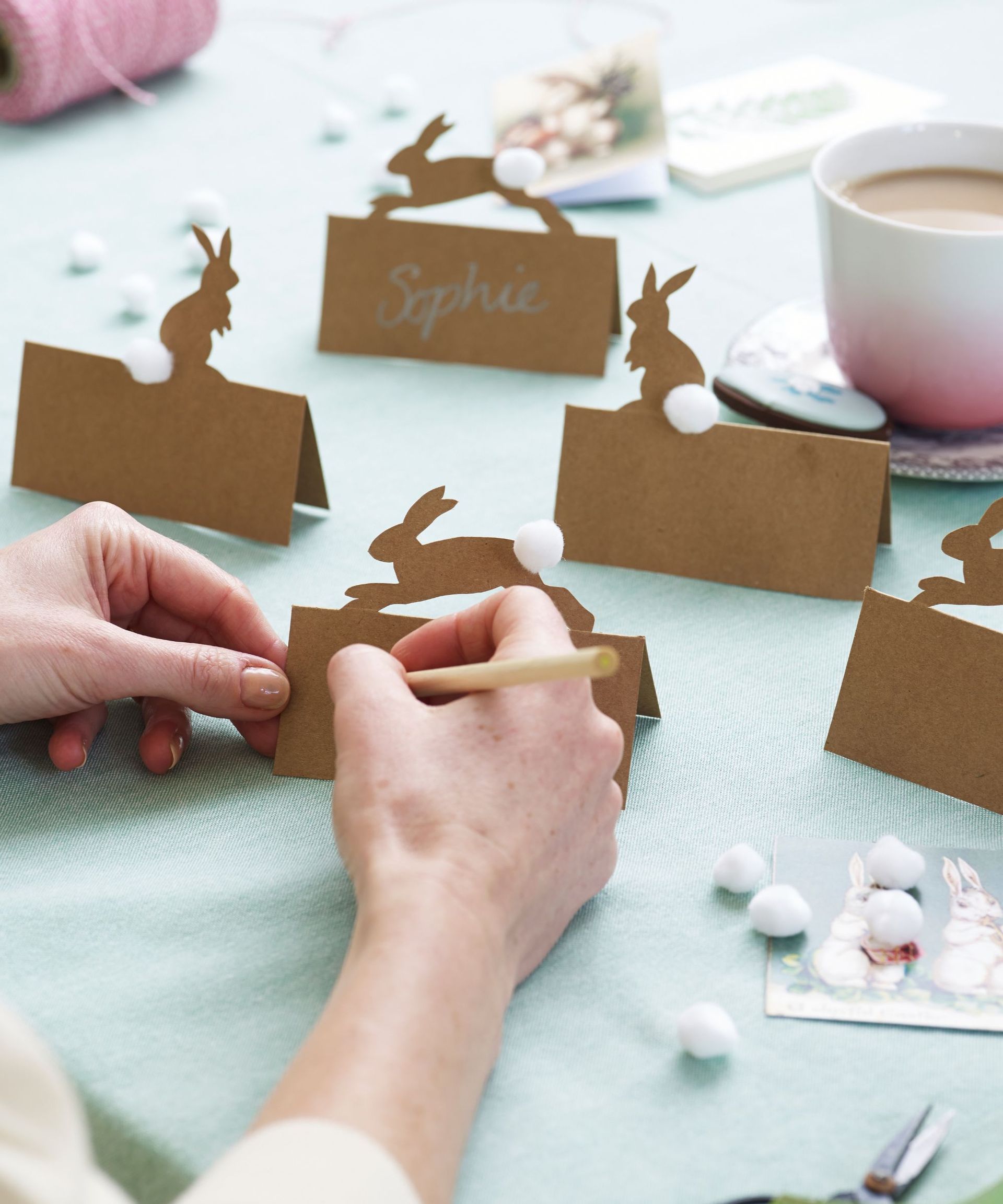 woman writing on brown kraft paper place cards with cut-out rabbit motifs and white pom pom tails