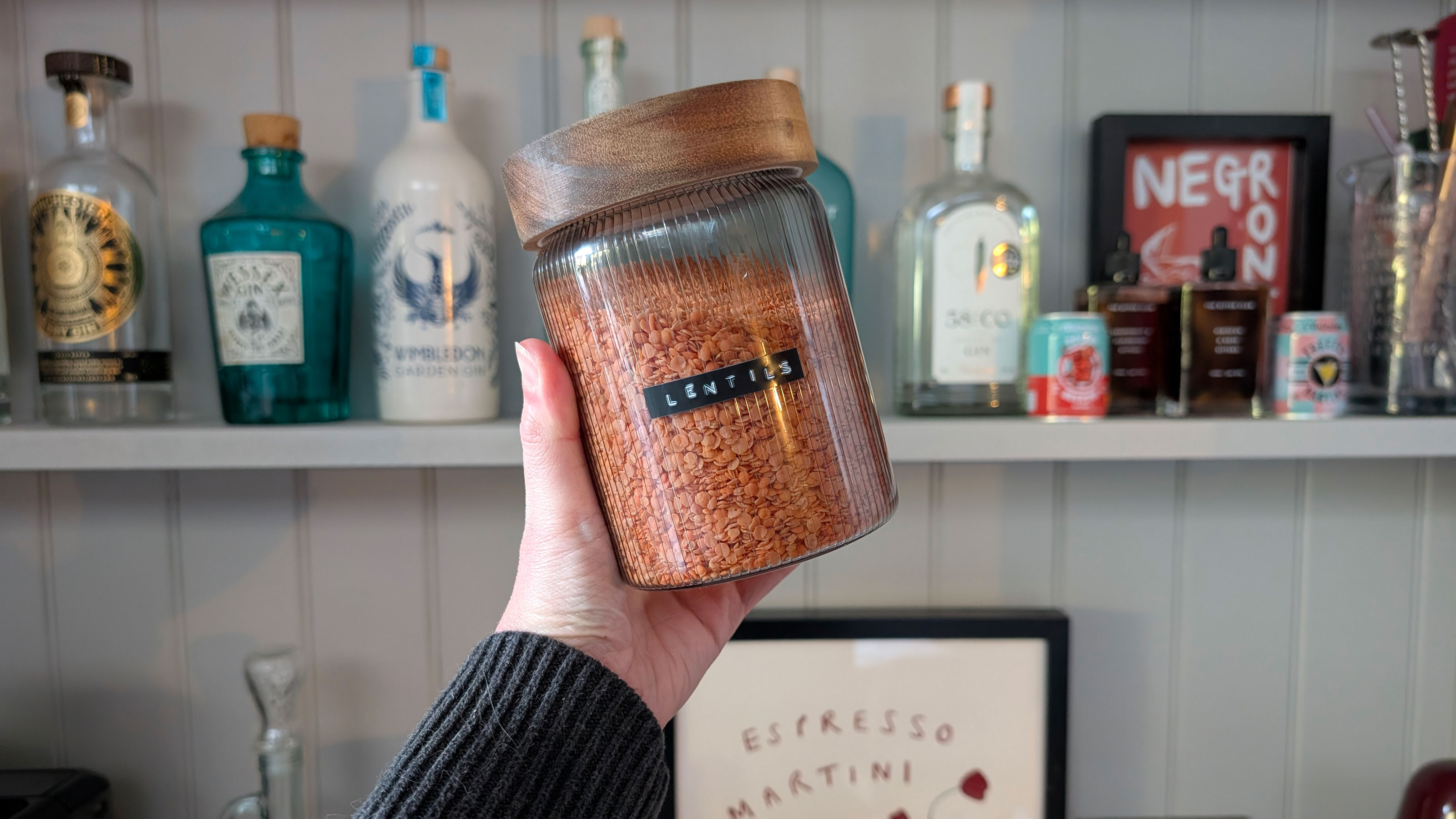 Woman's hand holding labelled jar of lentils in front of open bar shelving