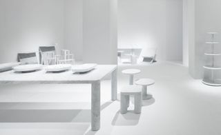 David Chipperfield's grand dining table, alongside three small chairs and stools, and James Irvine’s imaginative shelving. All in white.