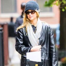 Jennifer Lawrence wears a gray beanie, gray scarf, black leather jacket.