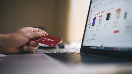 A hand holding a credit card in front of a laptop.