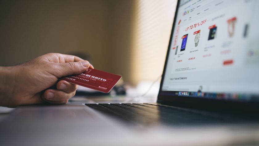 A hand holding a credit card in front of a laptop.