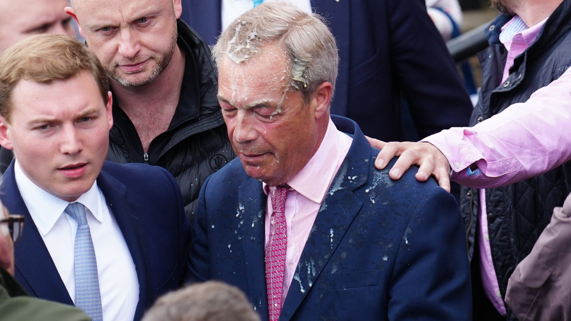 George Cottrell (L) looks on as Reform UK party leader Nigel Farage reacts after a woman threw what appeared to be a milkshake over him