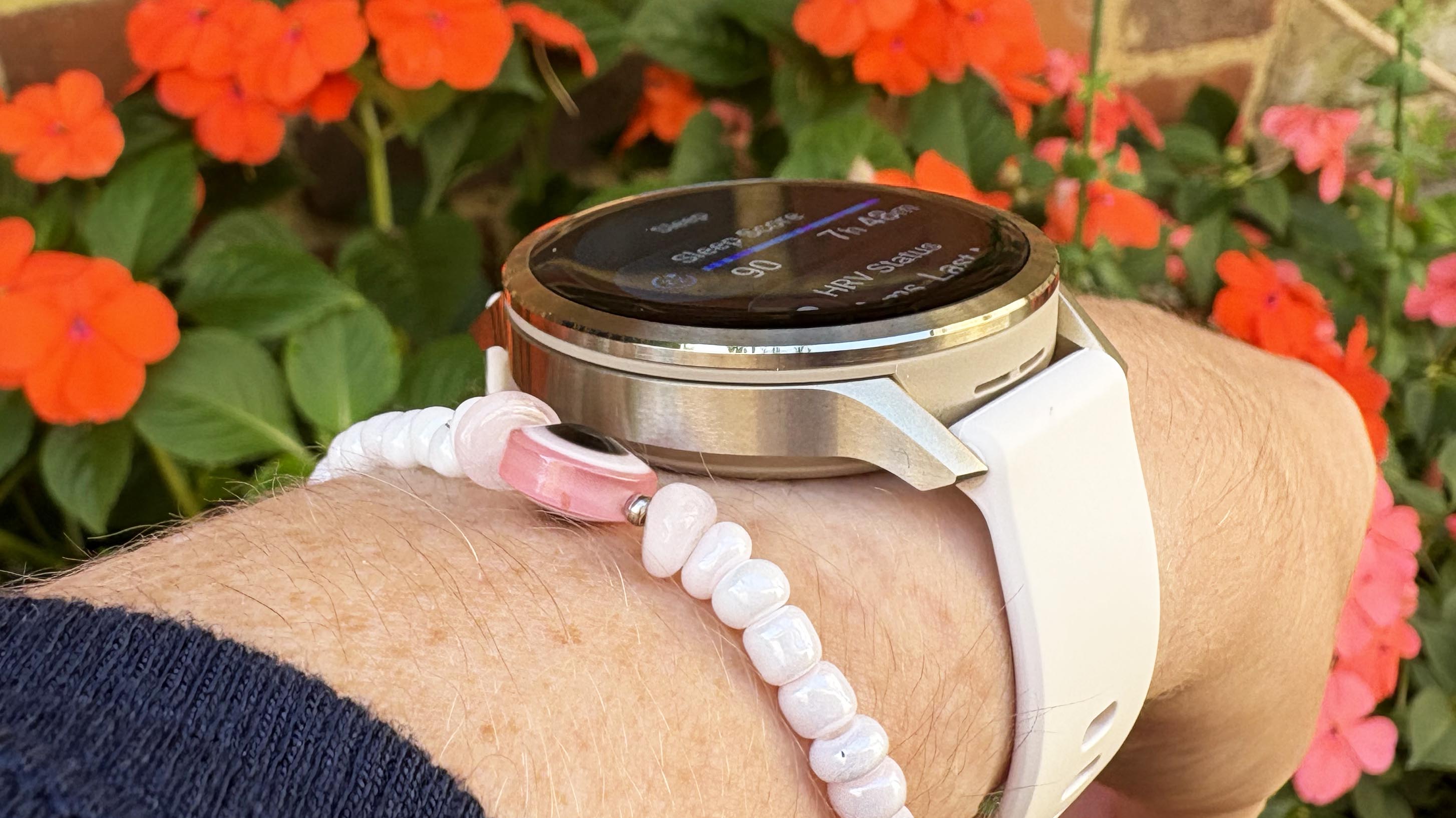 the Garmin Venu 4 in lunar gold on the wrist in front of some flowers