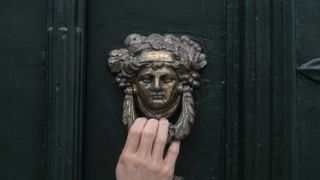 Hand touching a face shaped door knocker on black painted panelling