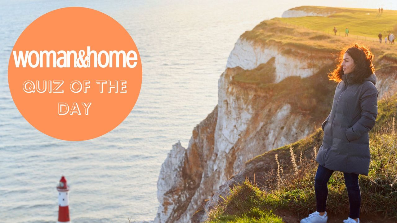 A woman stands at the top of a coastal path, looking out to sea, dressed in a warm winter coat. The woman&amp;home quiz of the day badge is over the photo