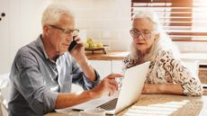 Elderly couple at their kitchen table with a laptop making a phone call