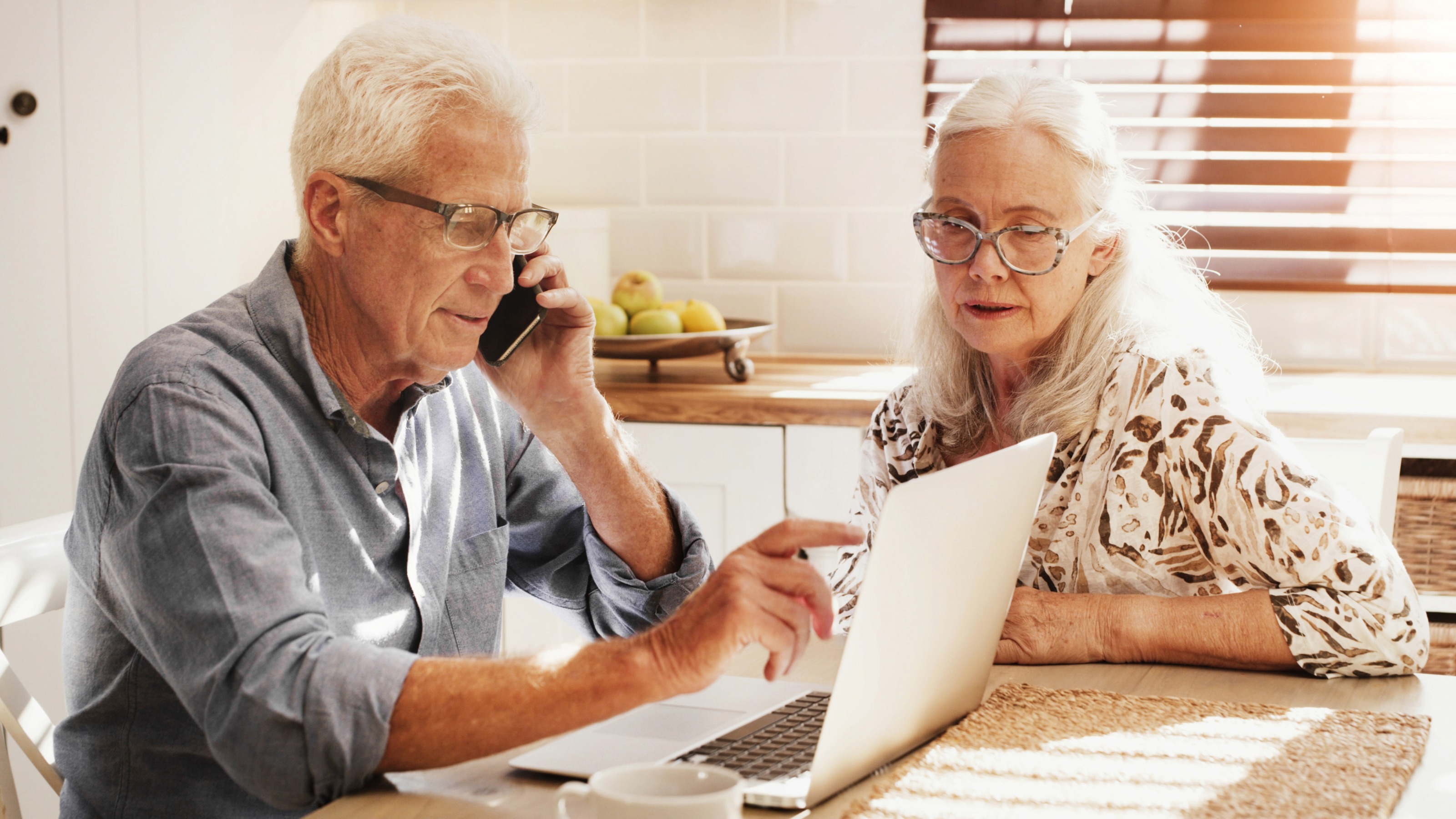Elderly couple at their kitchen table with a laptop making a phone call