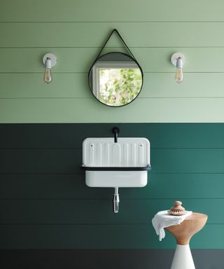 Two tone green bathroom walls, top half pale green, bottom dark green, small white basin, mirror, wall lights,