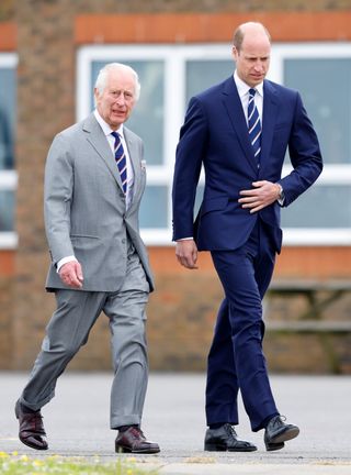 King Charles walking next to Prince William, both wearing suits and striped blue ties