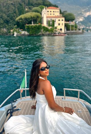 a photo showing what to wear on a boat with a woman wearing black sunglasses, with gold earrings, and a white maxi dress