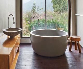 A freestanding bathtub in a small bathroom in front of a large window