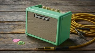 A Blackstar Fly 3 desktop guitar amp on a wooden floor with guitar cable, picks, and guitar cable