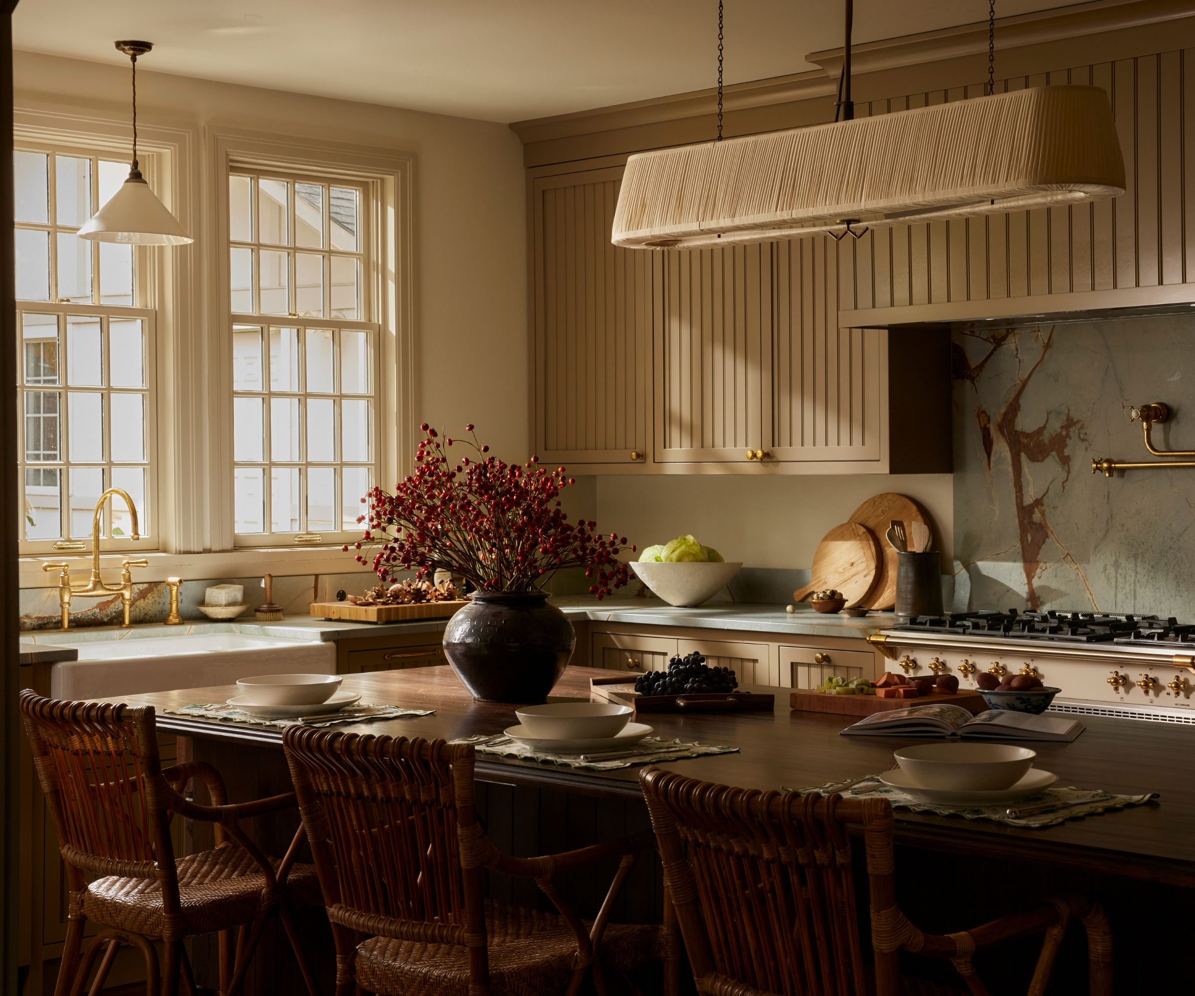A warm neutral kitchen with a ceramic pendant above the sink and a large pleated chandelier over the island