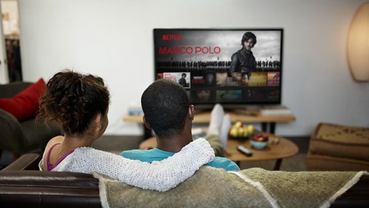 A man and a woman sit on a sofa to watch Netflix TV show Marco Polo on a television screen