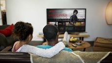 A man and a woman sit on a sofa to watch Netflix TV show Marco Polo on a television screen
