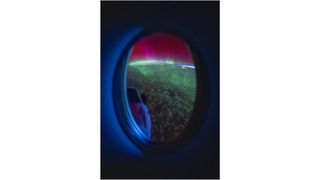 red and green auroral displays, seen through the window of a spacecraft orbiting earth