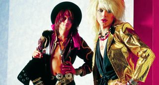 Hanoi Rocks' Andy McCoy [left] and Michael Monroe. Monroe wears a bright gold jacket and has blonde, '80s rock-sized hair. McCoy is cradling a black Gibson Firebird and weats a wide-brimmed hat.