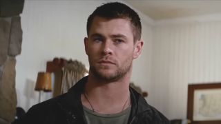 Chris Hemsworth standing in a living room with a determined look on his face in Red Dawn.