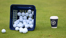 A bucket full of Titleist Pro V1 golf balls next to an Open mug
