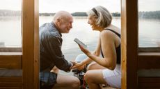 A couple laughing together sitting by the lake talking to family on the phone