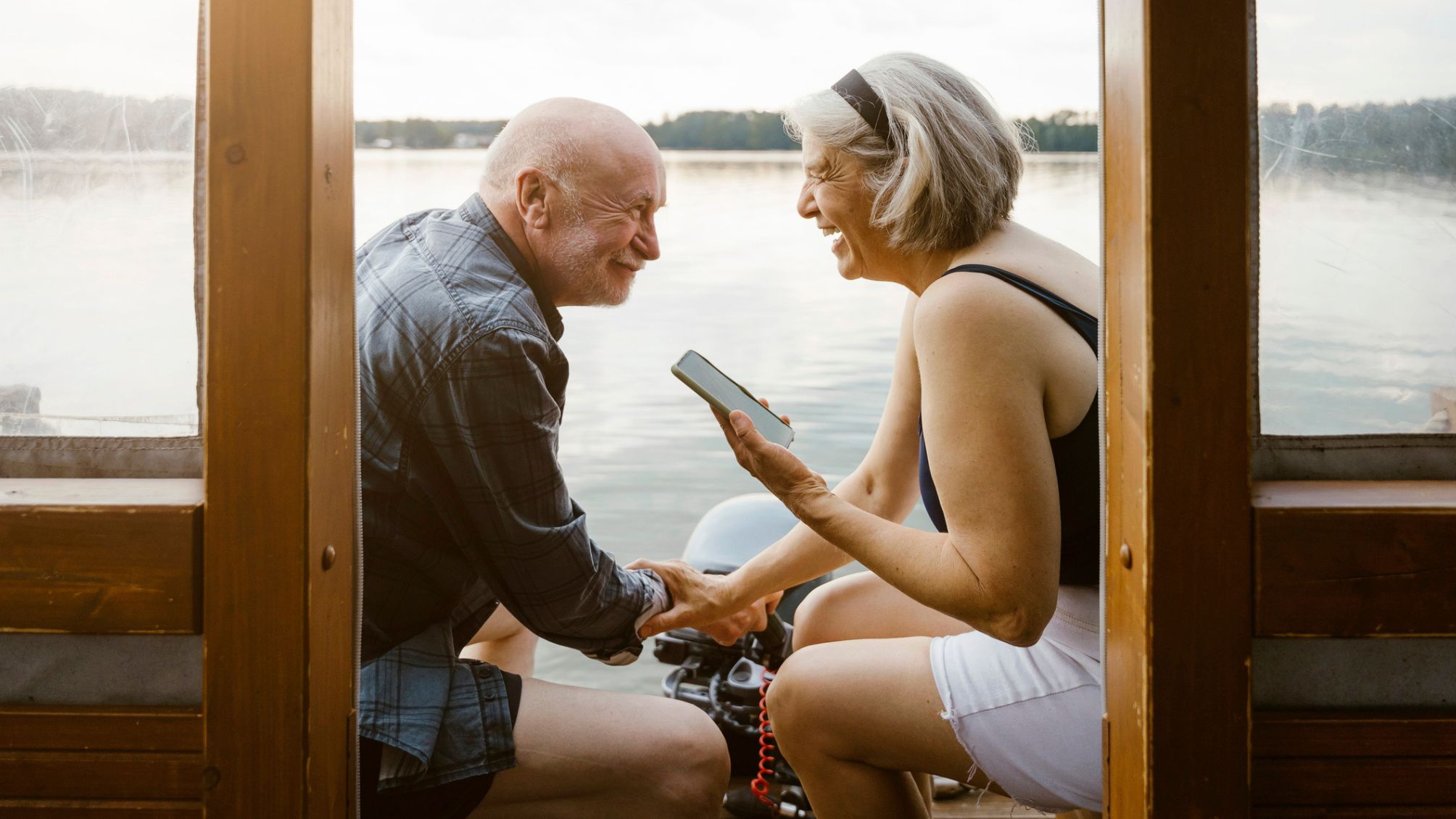A couple laughing together sitting by the lake talking to family on the phone