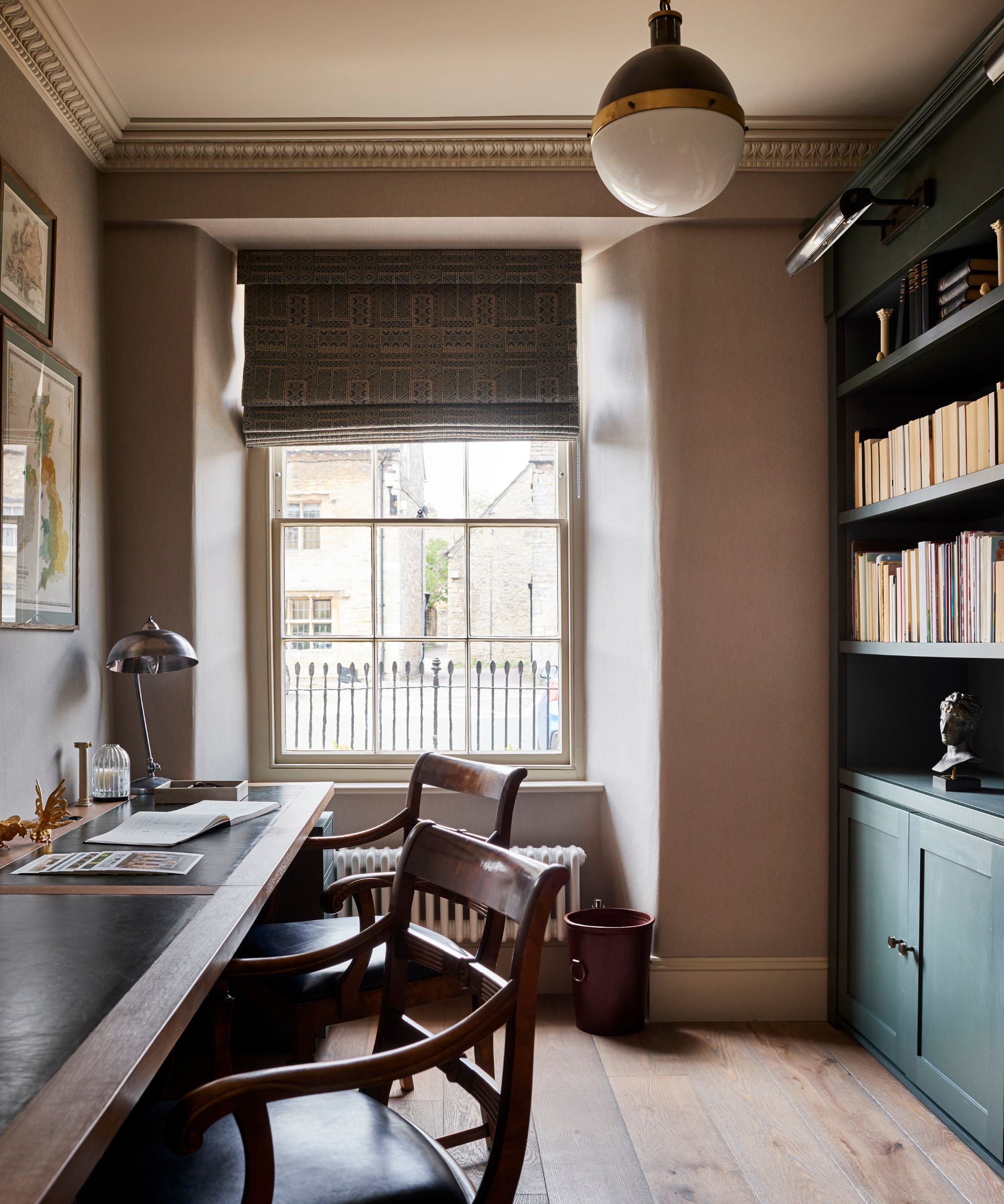 A warm, classic study with a wooden desk, vintage chairs, and bookcases, lit by a sash window and an elegant dome pendant ceiling light.