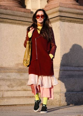 A woman wearing a layered look that incorporates a red coat, silk pink skirts and yellow tights