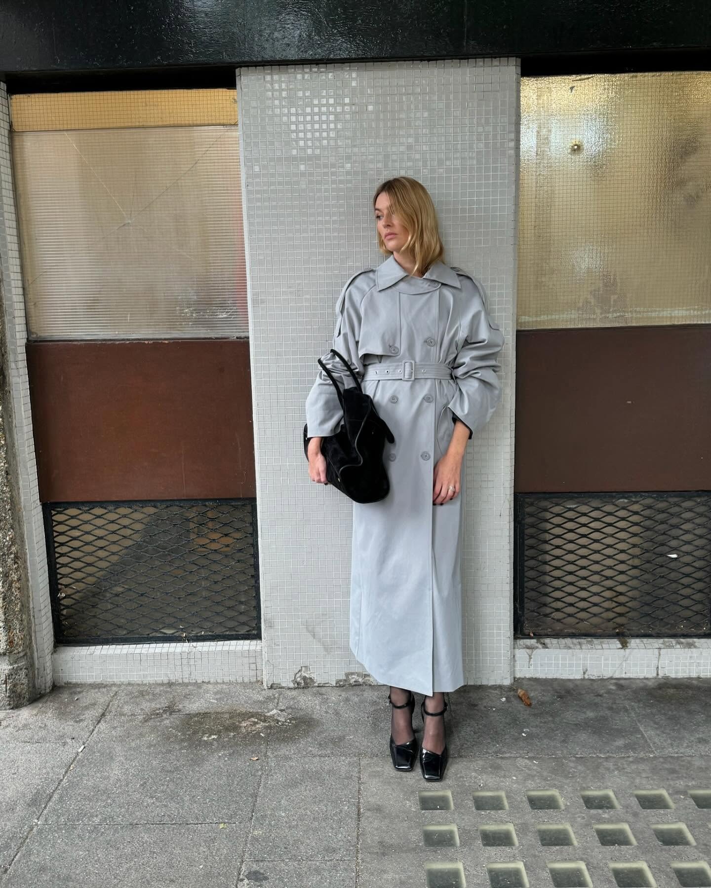 @camillecharriere wearing a gray trench coat with tights and pumps.