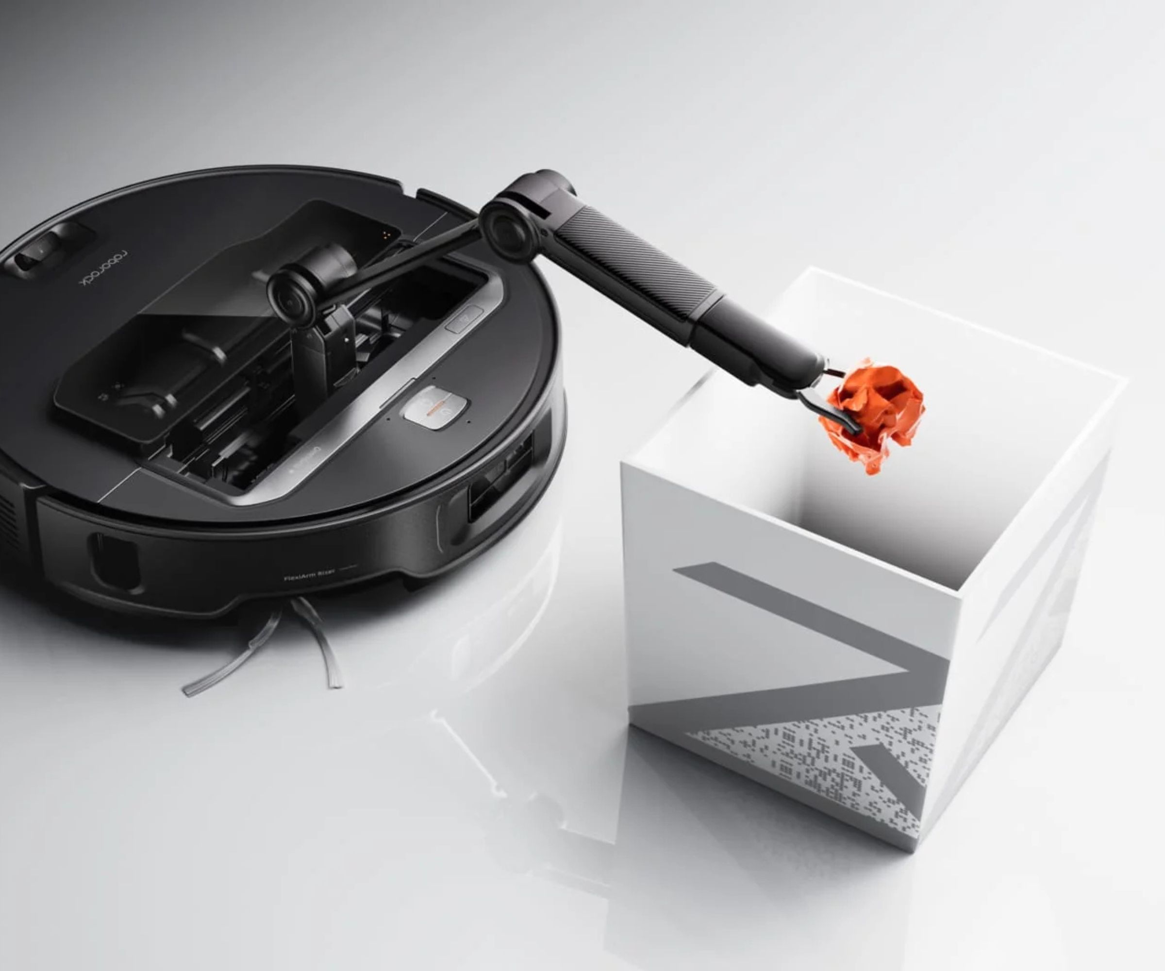 Roborock Saros Z70 holding crumpled orange paper above white trash can, on white reflective floor.