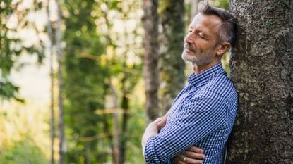 Man leaning against a tree in a forest