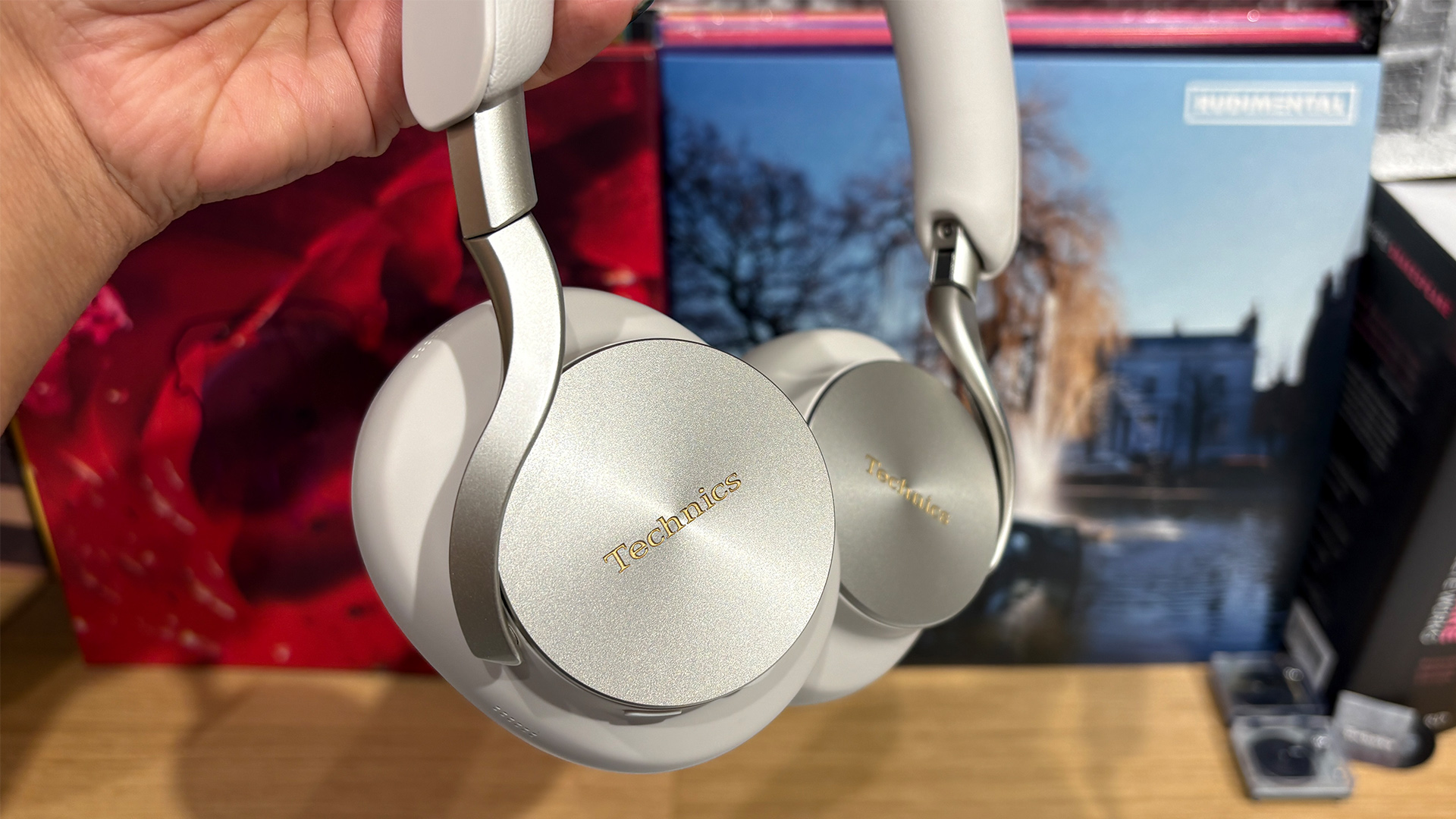Technics EAH-A1000 wireless over-ear headphones held in hand in front of busy bookcase