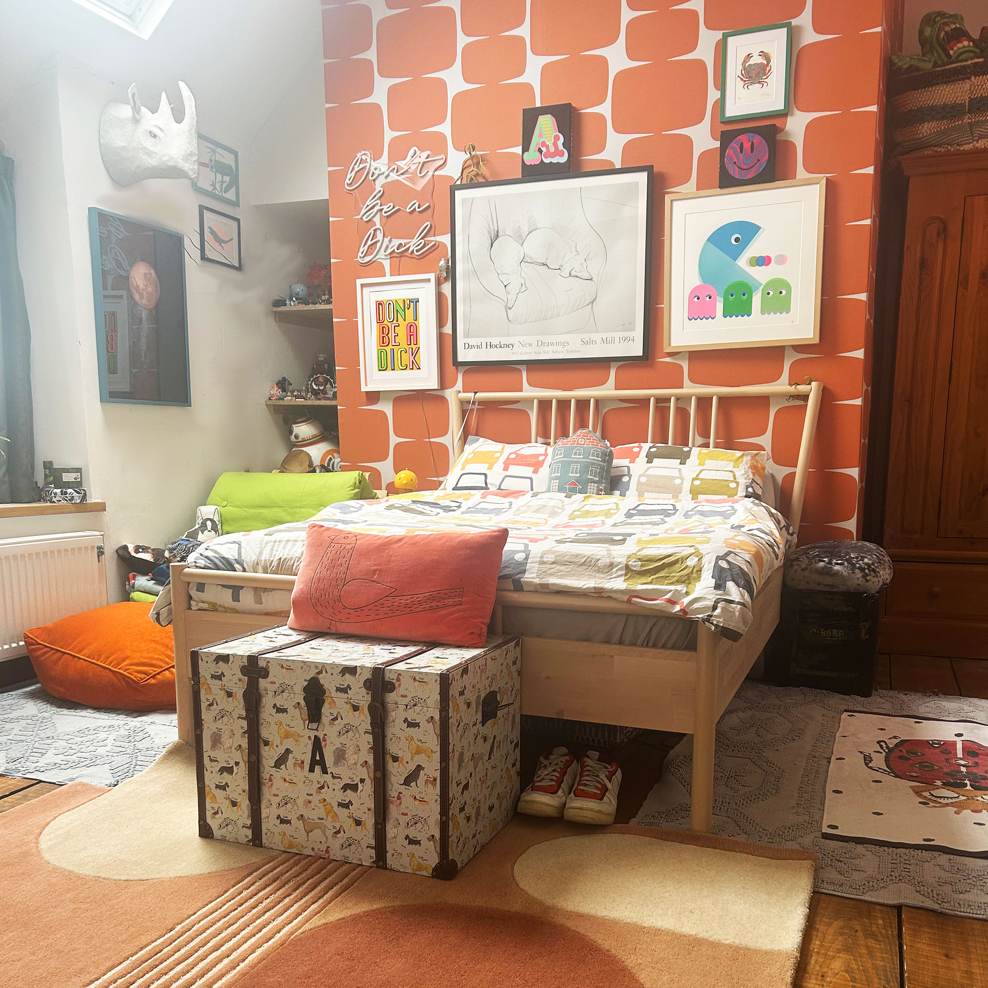 Teenage boy bedroom with orange patterned wallpaper feature wall covered with artwork behind bed