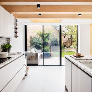 Views out onto a garden from a bright white kitchen with an oak beamed ceiling