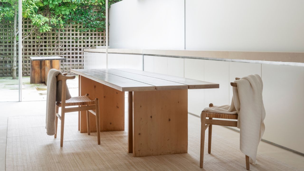 A minimalist house features a wooden table and patching wooden chair covered in cashmere throws in neutral tones.