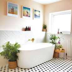 Pale pink and white bathroom with freestanding bathtub and herringbone patterned wall tiles