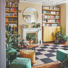 A living room with yellow bookcases matching the yellow walls and a chequerboard rug on the floor