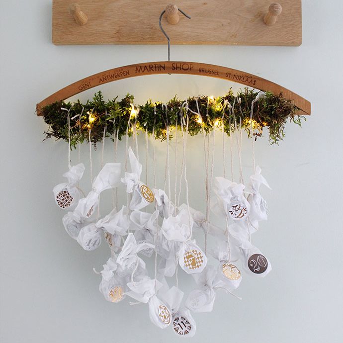 white wall with wooden set of three pegs and a handmade advent calendar hung from a vintage clothes hanger