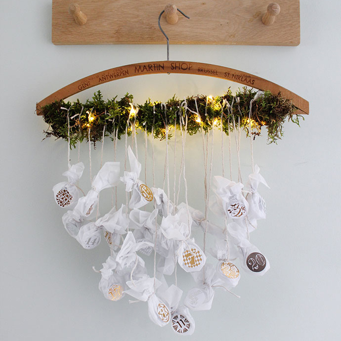 white wall with wooden set of three pegs and a handmade advent calendar hung from a vintage clothes hanger